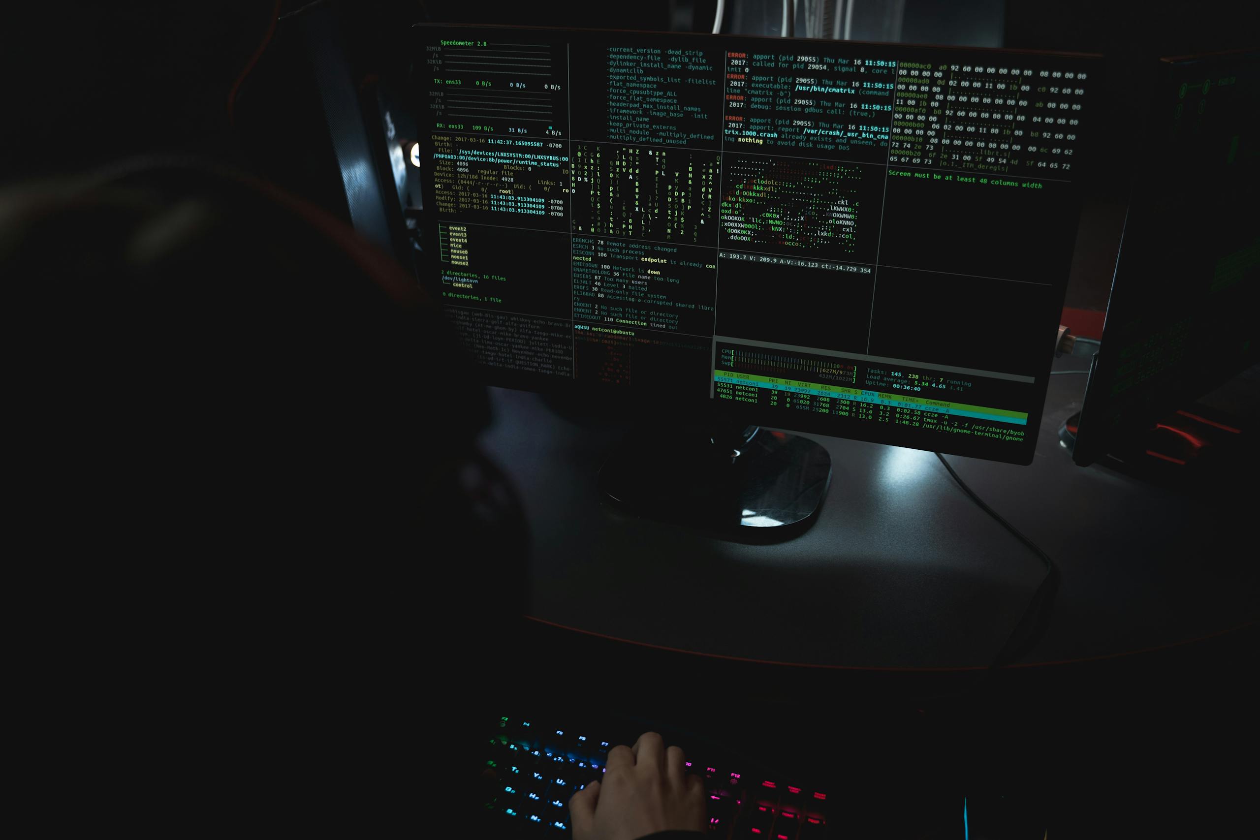 Dark room setup with code displayed on PC monitors highlighting cybersecurity themes.